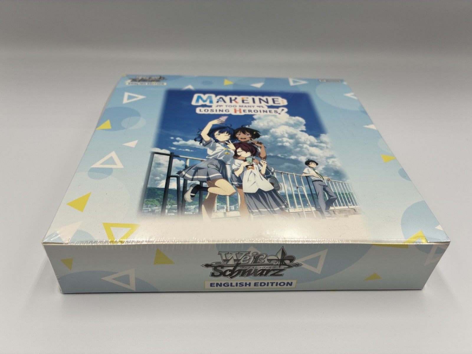 A boxed anime card game titled Too Many Losing Heroines English Edition, photographed on a light gray studio background. The box features illustrated anime characters on the front and a blue sky-themed design with geometric accents.