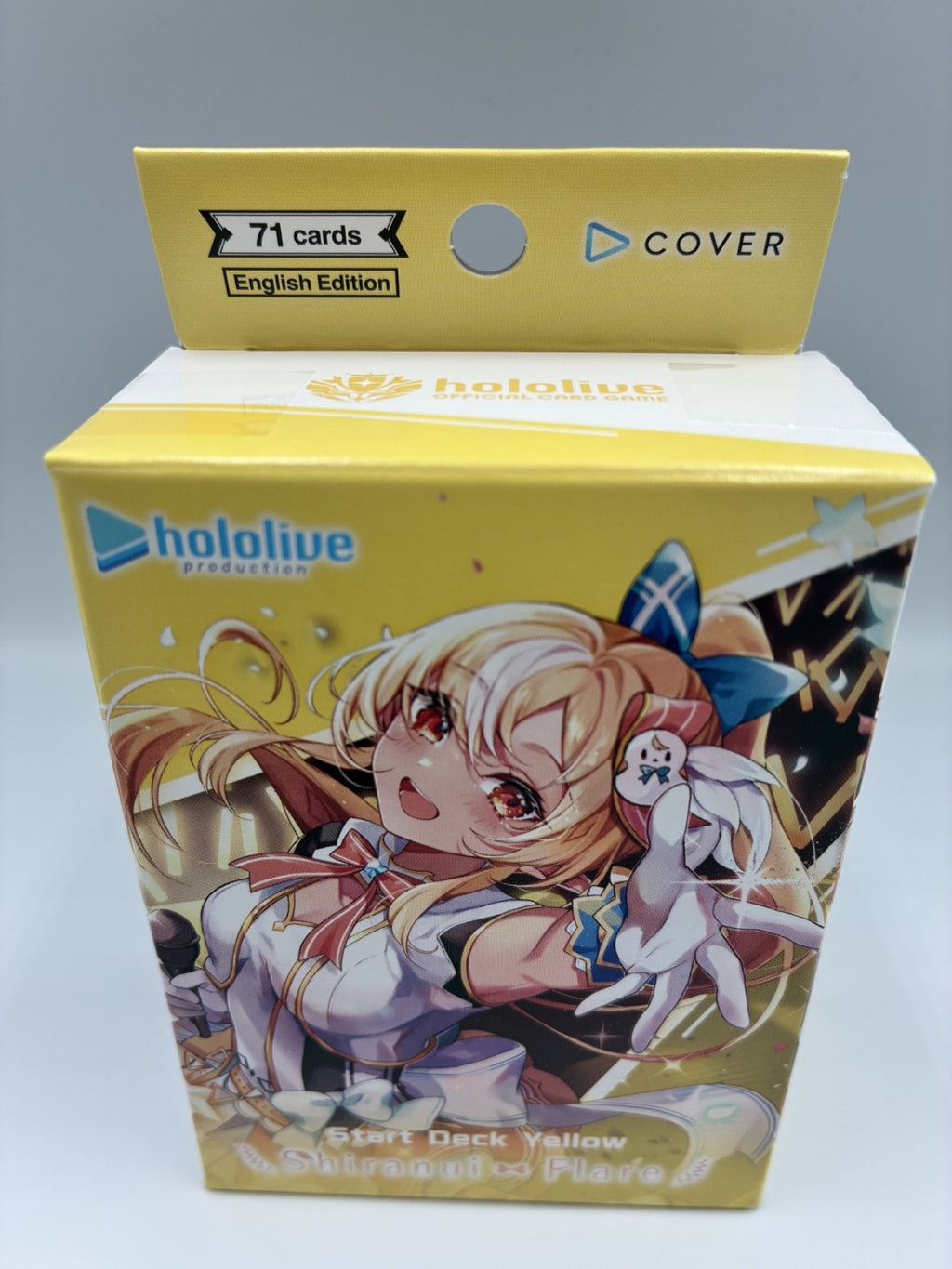 A yellow Hololive Production card deck box for the 'Start Deck Yellow' 'Shimmer of Flames' English Edition, featuring anime character artwork of a blonde girl and a white rabbit on the front.