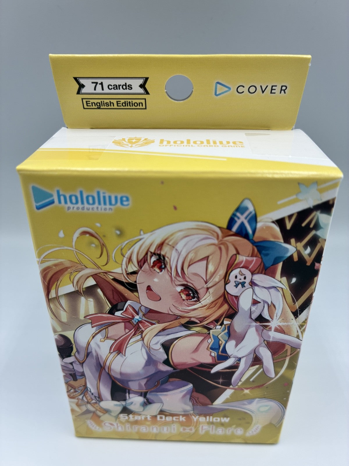 A yellow Hololive Production card deck box for the 'Start Deck Yellow' 'Shimmer of Flames' English Edition, featuring anime character artwork of a blonde girl and a white rabbit on the front.
