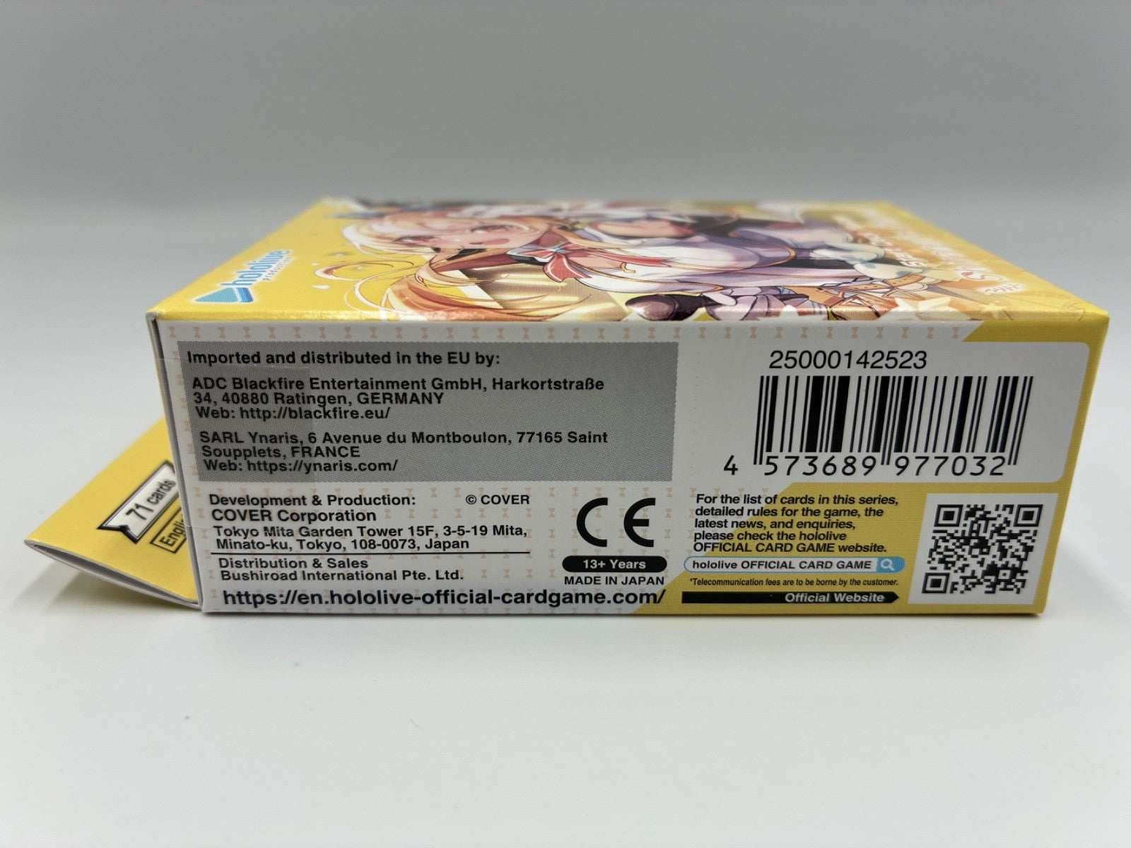 The back of a yellow and white box for the card game, showing printed text, a barcode, a QR code, and an illustration of anime characters on a light gray background.